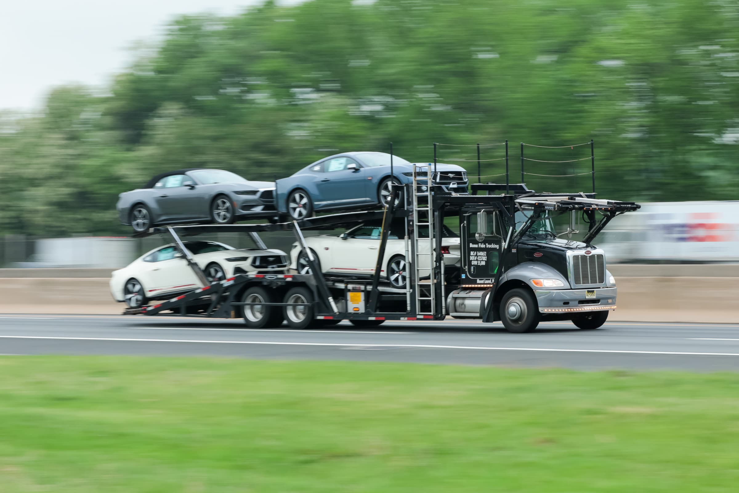 Car carrier truck transporting multiple vehicles on a two-level trailer driving on highway with green foliage in background